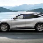 A white 2021 Ford Mustang Mach-E drives past a lake after leaving the electric car dealer.