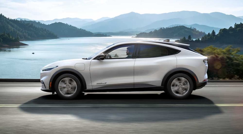 A white 2021 Ford Mustang Mach-E drives past a lake after leaving the electric car dealer.