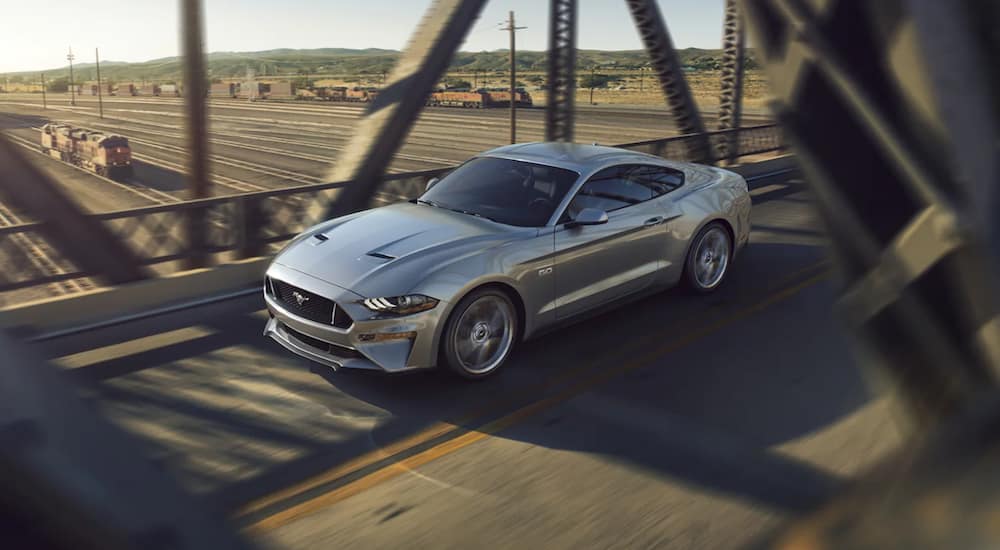 A silver 2021 Ford Mustang is driving over a bridge.
