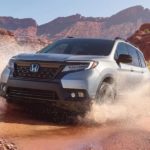 A silver 2021 Honda Passport is shown driving through a puddle in the desert.