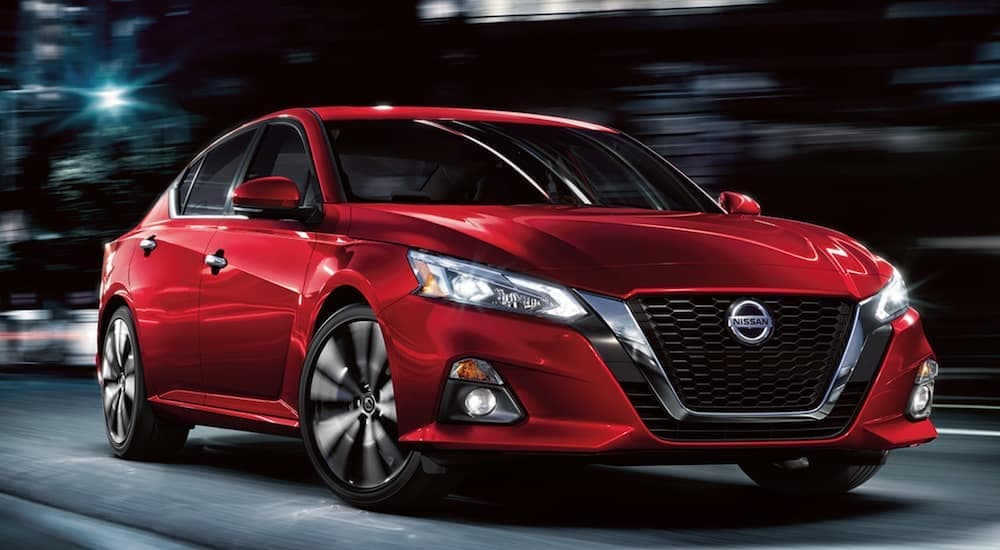 A red 2021 Nissan Altima is shown driving through a city at night.
