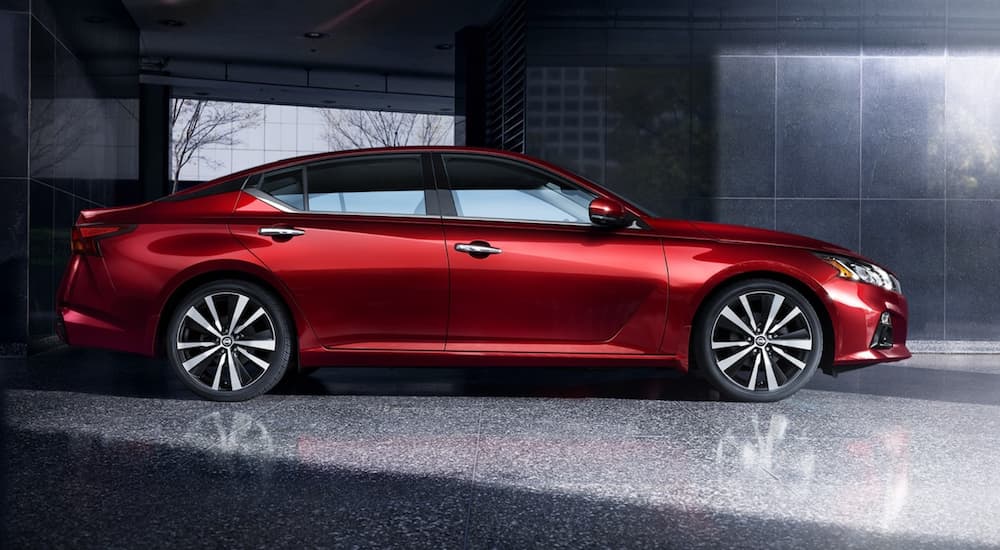 A red 2021 Nissan Altima is shown from the side in a modern gallery.
