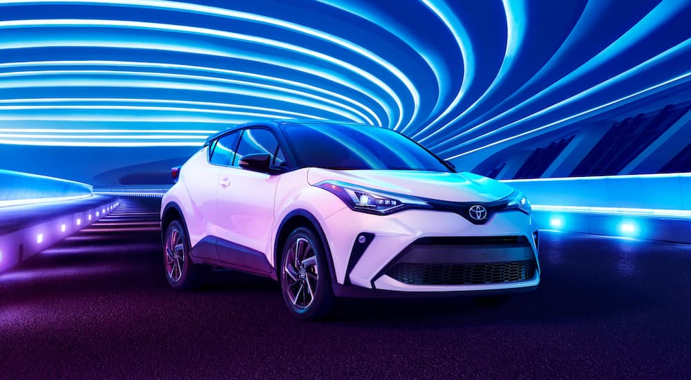 A white 2021 Toyota C-HR is parked in a modern gallery with blue and purple led lighting.
