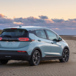 A light blue 2022 Chevy Bolt EV is shown angled right parked on a beach at sunset.