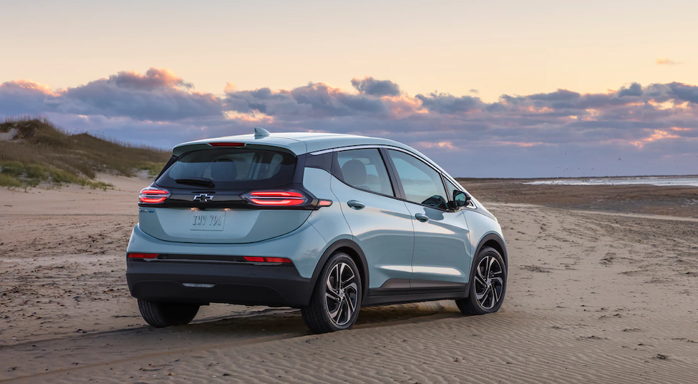 A light blue 2022 Chevy Bolt EV is shown angled right parked on a beach at sunset.