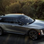 A silver 2023 Cadillac Lyriq is shown from the side driving down a country road.