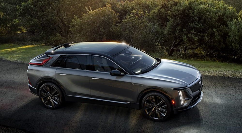 A silver 2023 Cadillac Lyriq is shown from the side driving down a country road.