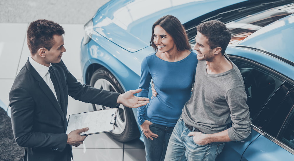 A car salesman is talking to a couple purchasing a car.