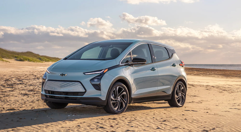 A light blue 2022 Chevy Bolt EV is parked on a beach after leaving a Chevy dealership.