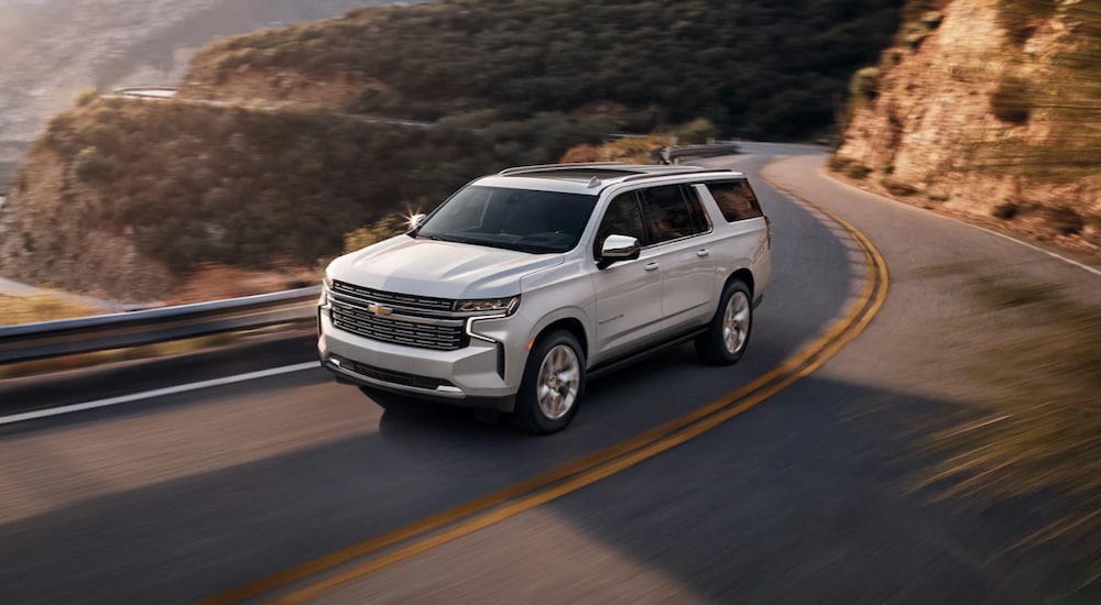 A white 2021 Chevy Suburban is shown from the side driving down a two way road.