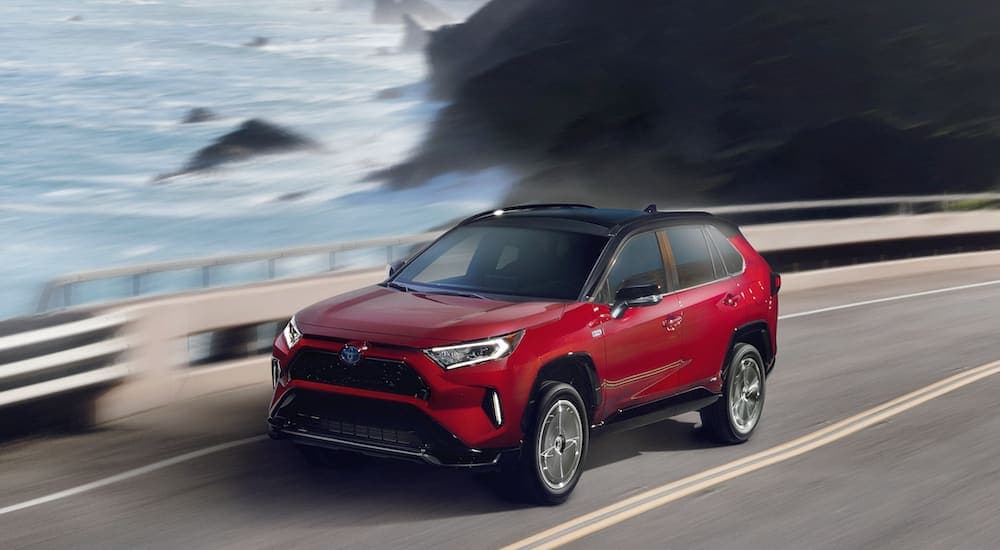 A red 2021 RAV4 Prime is driving past a lake after leaving a Ford Escape dealership.