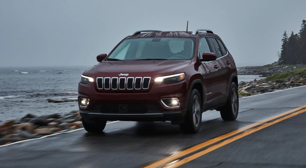 A red 2021 Jeep Cherokee is driving on a two lane road next to the ocean after reviewing the Jeep Cherokee buyers guide.