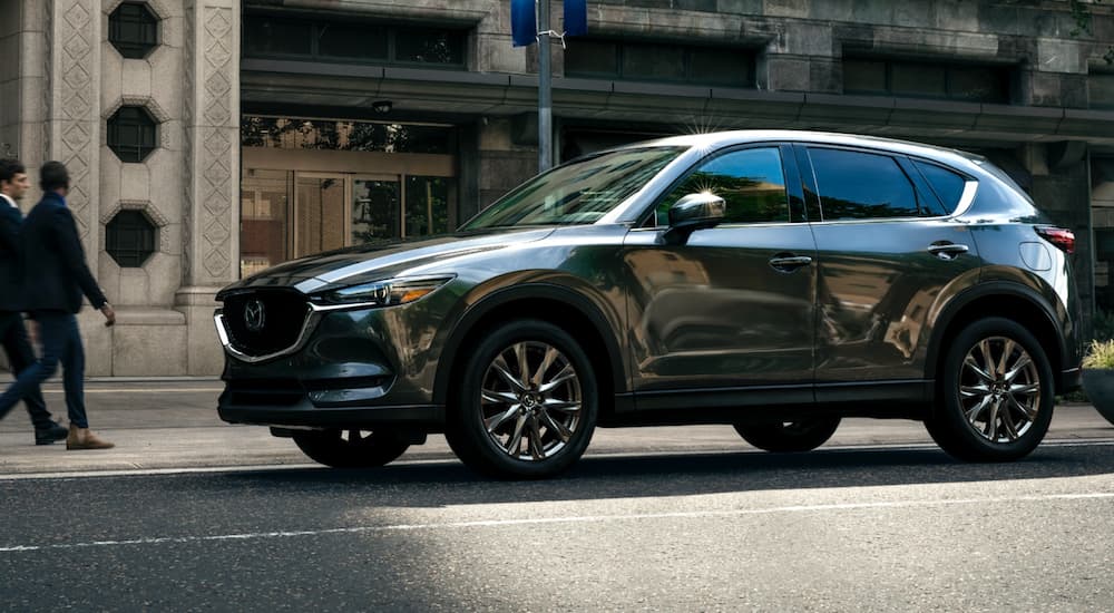 A green 2021 Mazda CX-5 is parked outside of a high end store.