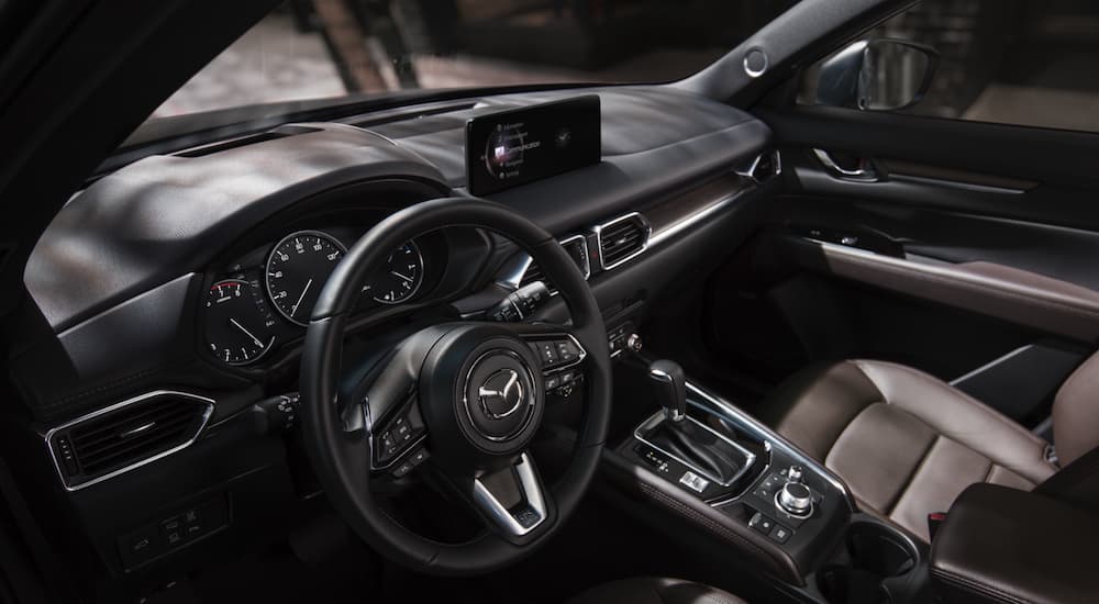 The interior of a 2021 Mazda CX-5 shows the steering wheel and infotainment screen.