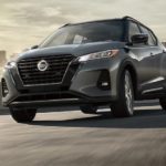 A grey 2021 Nissan Kicks is driving on a highway past a city.