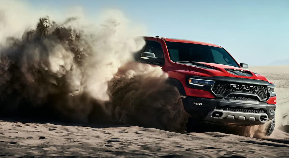 A red 2021 Ram 1500 TRX is kicking up sand while off-roading on a dune.