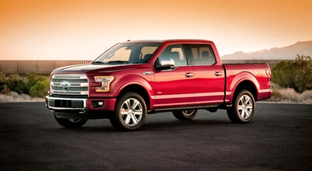 A red 2015 Ford F-150 is parked on pavement in front of mountains.