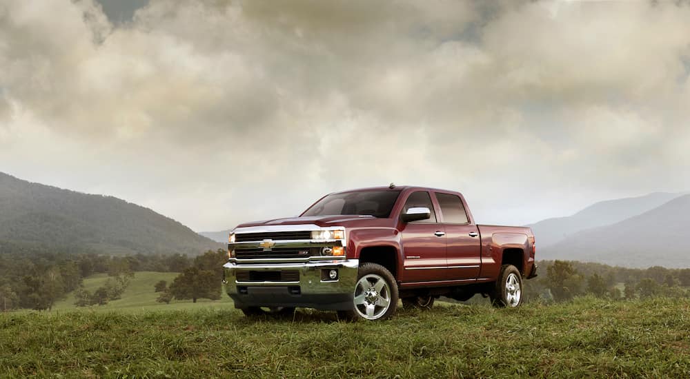A red 2015 Chevy Silverado 2500 HD LTZ is parked in the grass in front of mountains.