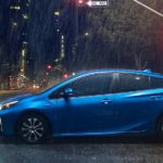 A blue 2021 Toyota Prius is stopped at a traffic light in the rain after leaving a used Toyota Dealer