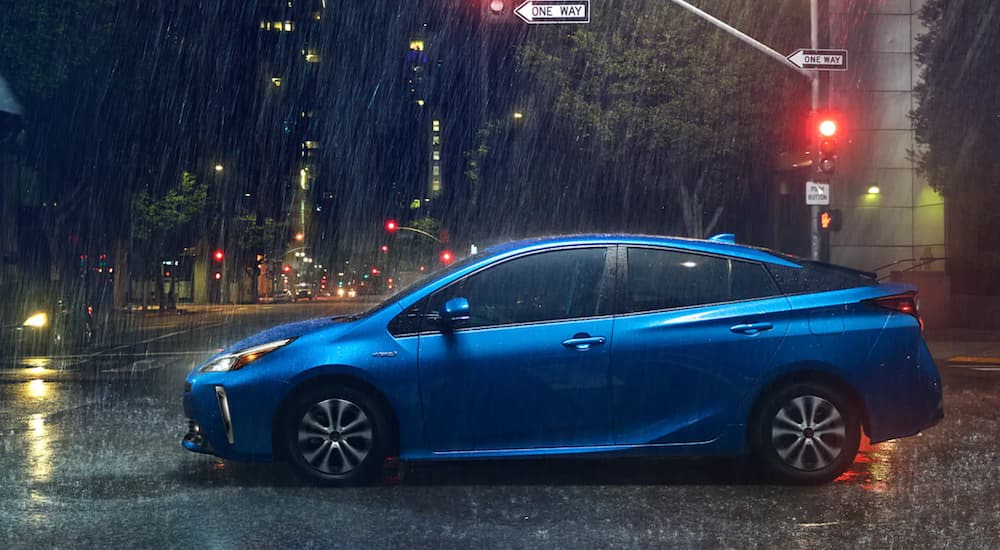 A blue 2021 Toyota Prius is stopped at a traffic light in the rain after leaving a used Toyota Dealer