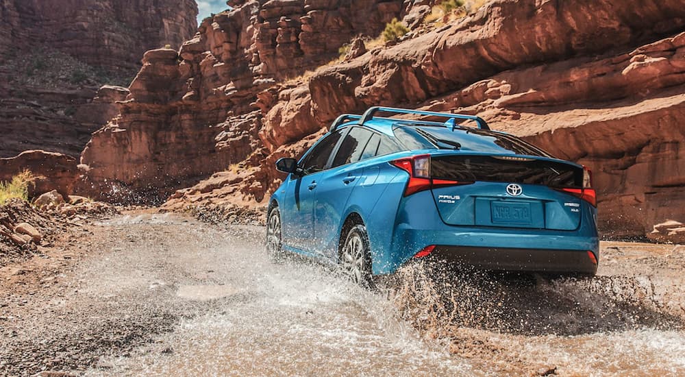 A light blue 2021 Toyota Prius is driving past a desert mountain. 