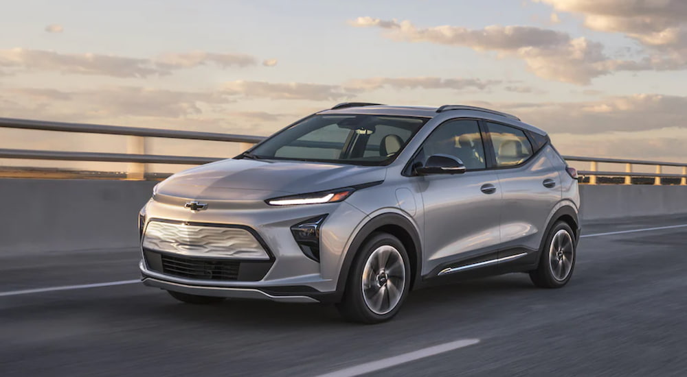 A silver 2022 Chevy Bolt EUV is shown from the side driving over a bridge at sunset after leaving an electric car dealer.