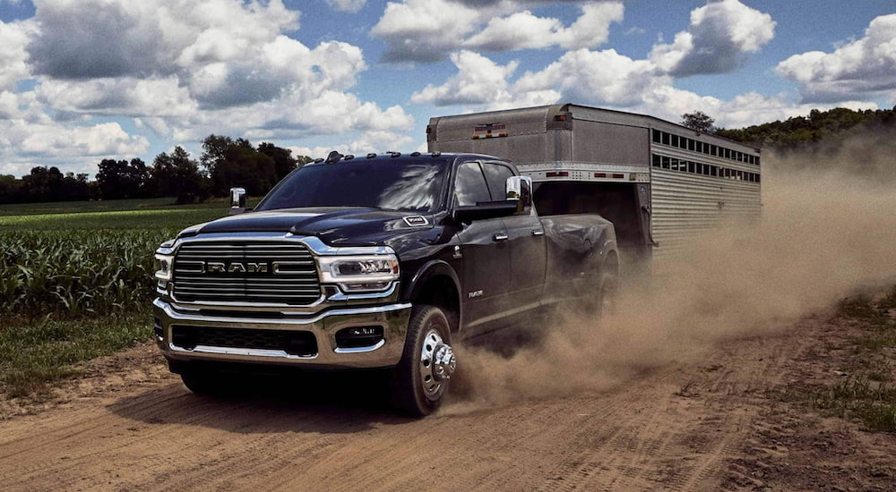 A blue 2020 Ram 3500 is towing a closed trailer down a dirt road.