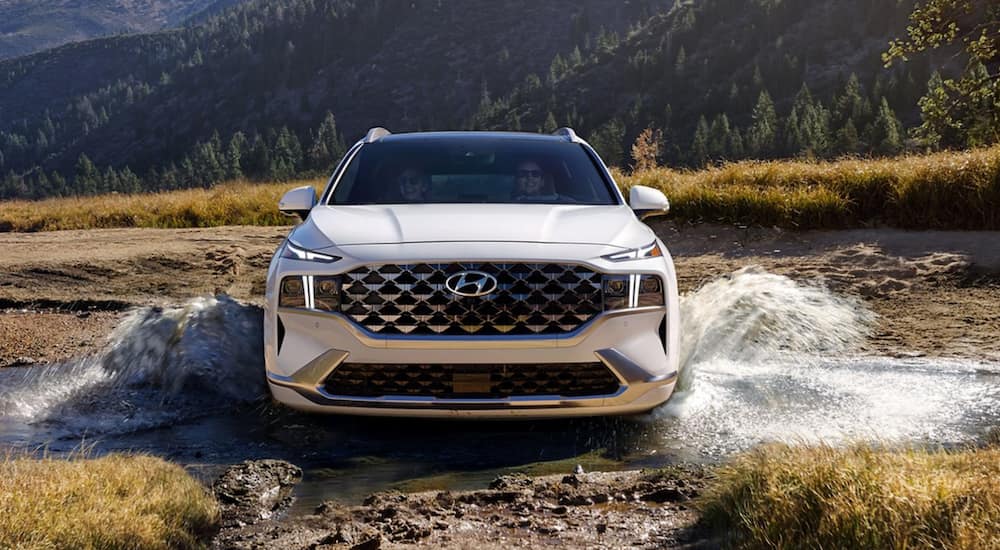 A white 2021 Hyundai Santa Fe is driving through a muddy field.