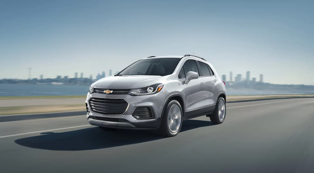 A grey 2021 Chevy Trax is driving over a bridge past a city.