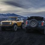 A blue and a yellow 2021 Ford Bronco are parked in a field at sunset after winning a 2021 Ford Bronco vs 2021 Toyota 4Runner comparison.