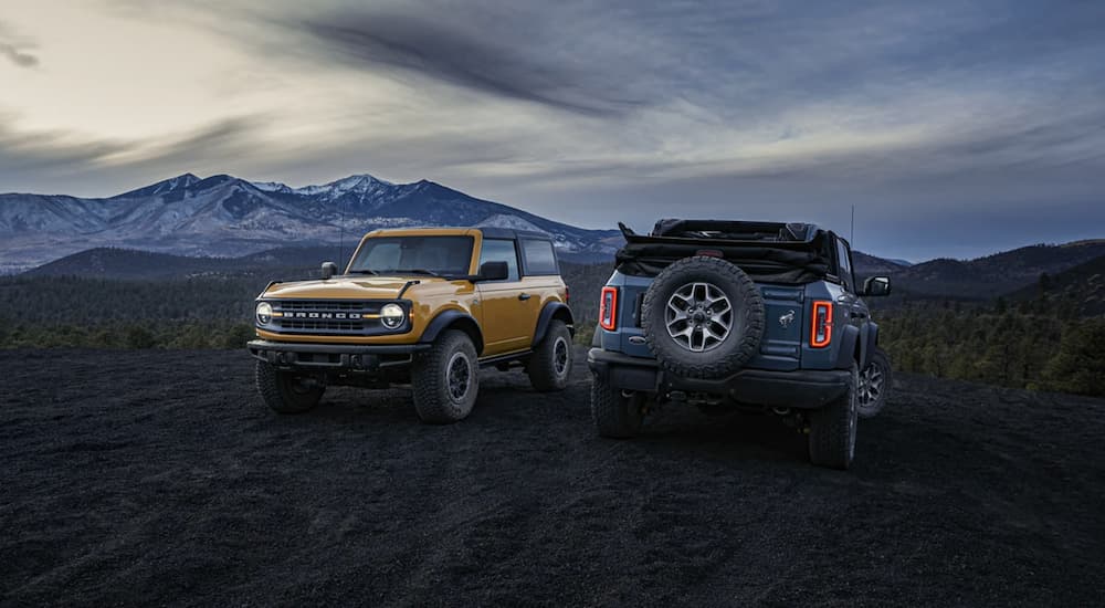 A blue and a yellow 2021 Ford Bronco are parked in a field at sunset after winning a 2021 Ford Bronco vs 2021 Toyota 4Runner comparison.