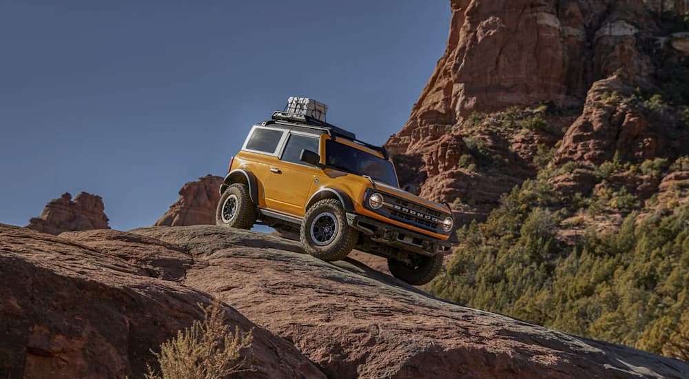 A yellow 2021 Ford Bronco is shown off-roading on large rocks in the desert.