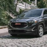 A green 2021 GMC Terrain is driving down a cobblestone road after winning a 2021 GMC Terrain vs 2021 Jeep Compass comparison.