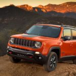 An orange 2021 Jeep Renegade is parked on a dirt hill in the mountains at sunset.