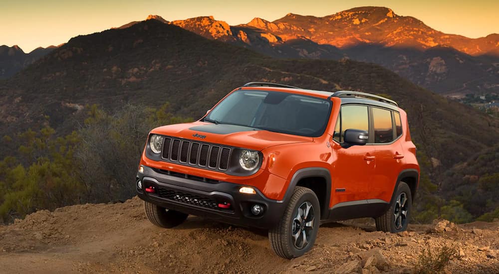 An orange 2021 Jeep Renegade is parked on a dirt hill in the mountains at sunset.