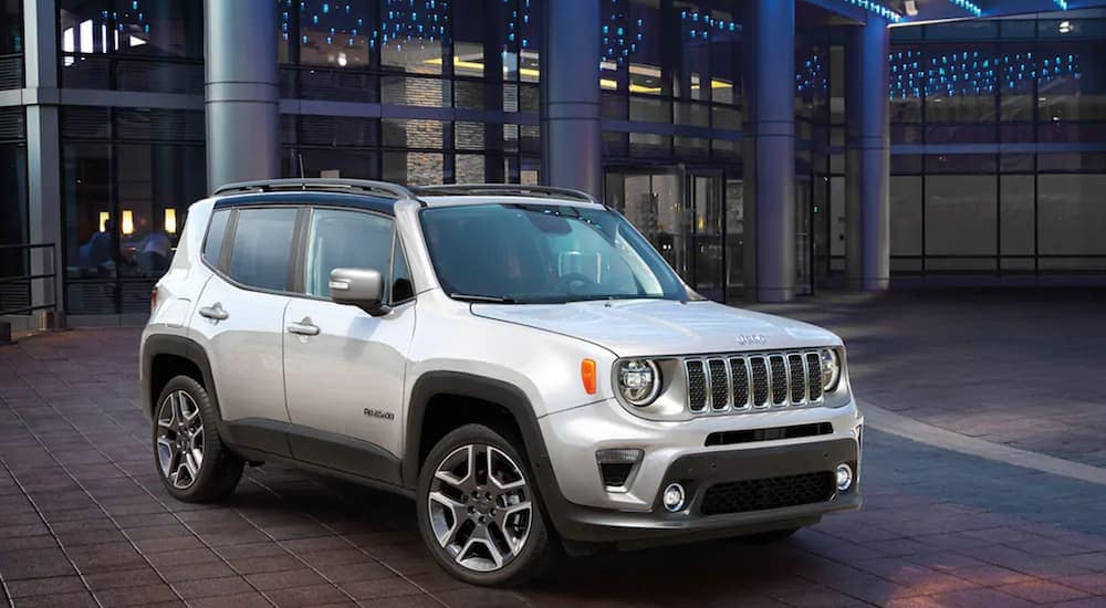 A silver 2021 Jeep Renegade is parked in front of a modern building.