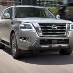 A silver 2021 Nissan Armada is shown from the front driving through a city.