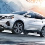 A white 2021 Nissan Murano is shown driving on a snowy road.