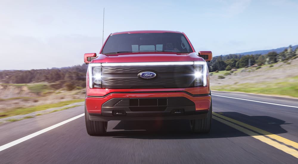 A red 2022 Ford F-150 Lightning Lariat is shown from the front driving down a road.