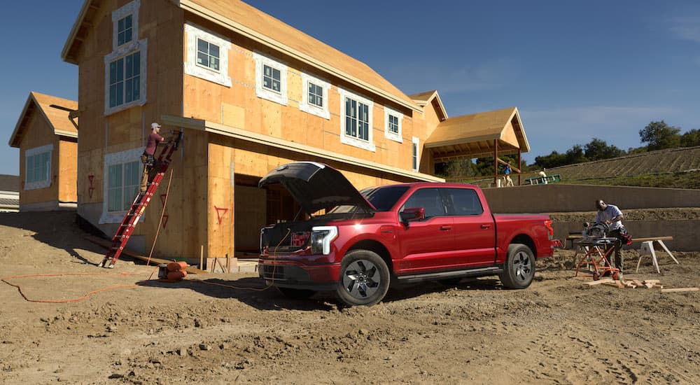 A red 2022 Ford F-150 Lightning Platinum is shown from the side parked next to an unfinished house.