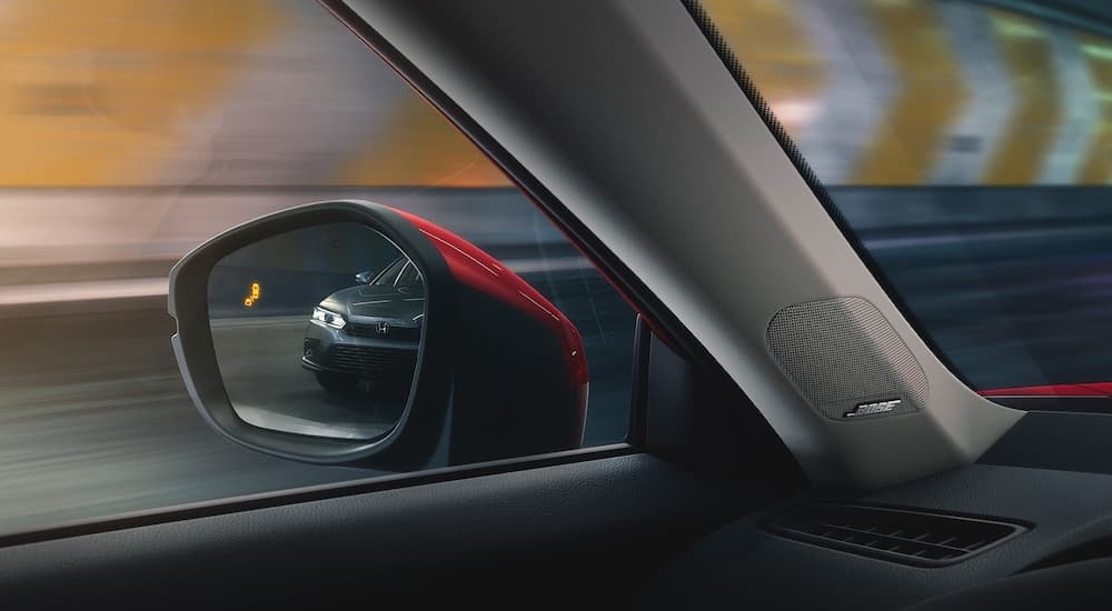 A close up shows the blind spot monitoring icon on the mirror of a red 2022 Honda Civic.