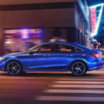 A blue 2022 Honda Civic Touring is shown from the side driving through a city at night.