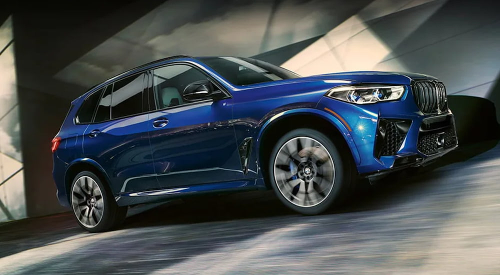 A blue 2019 BMW 3X M Series is shown from an angle driving on cement.