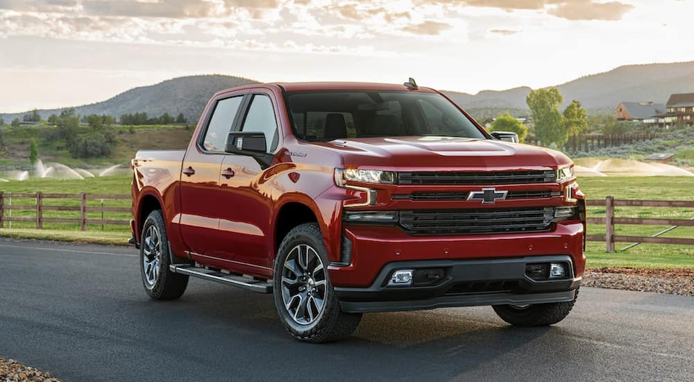 A red 2021 Chevy Silverado is parked on a paved road next to a field.