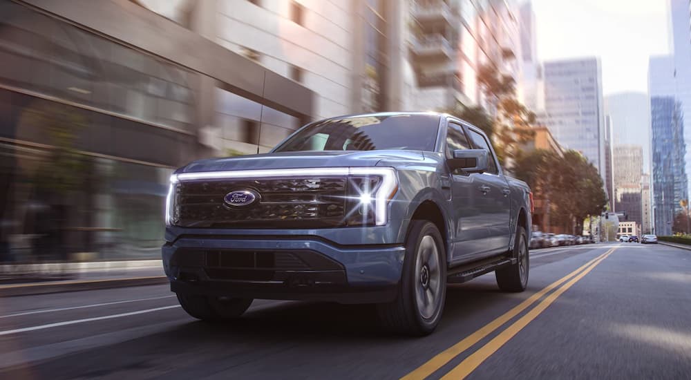 A blue 2022 Ford-150 Lightning is driving through a city.