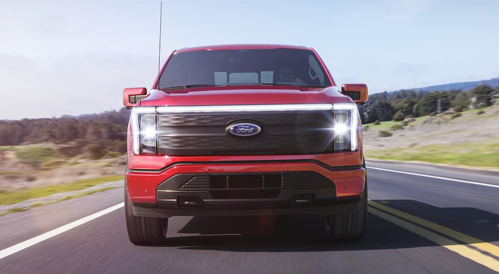 A red 2022 Ford F-150 Lightning is driving down a two lane road.