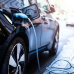 A black electric car is charging while the driver catches up on the current auto news.