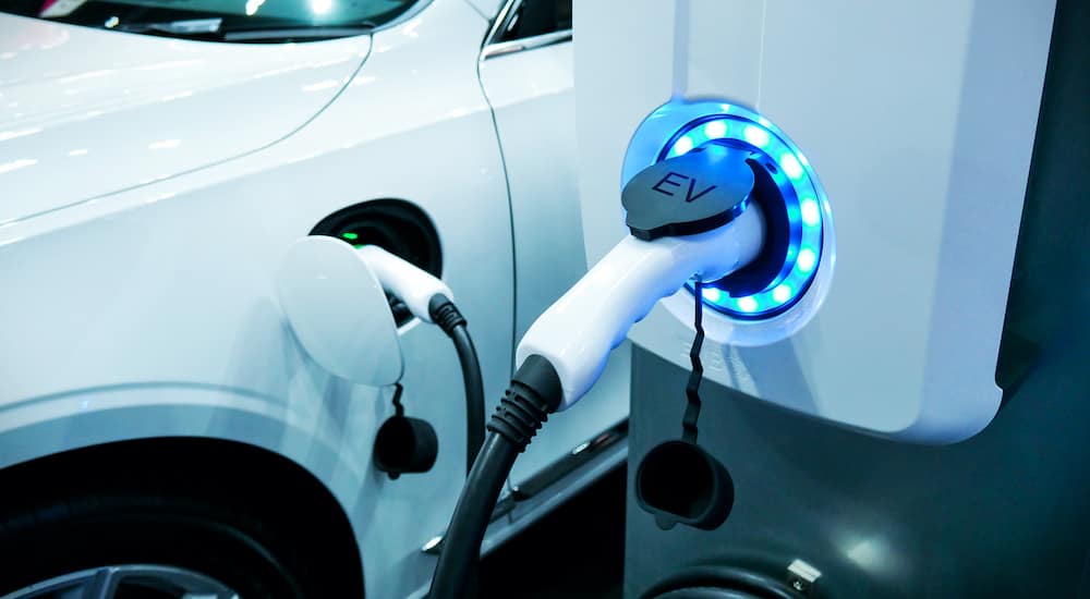 A white electric car is charging at a charging station.