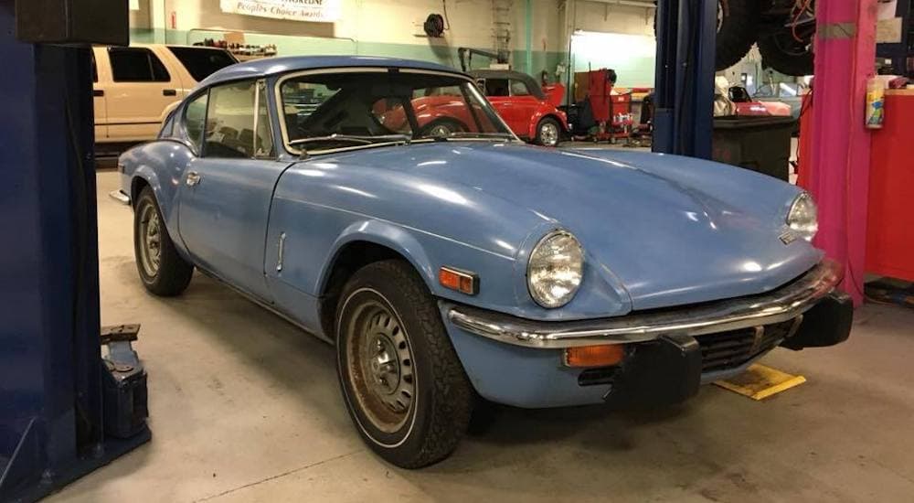 A blue 1975 Triumph Spitfire is shown parked between lift posts.