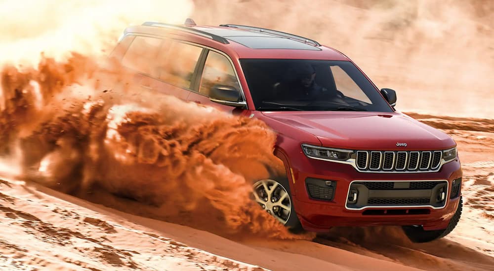 A red 2021 Jeep Grand Cherokee L is driving through a sandy desert.